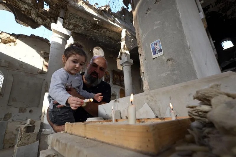 Християнин тримає свою дочку, поки вони запалюють свічки біля вівтаря грецької православної церкви Святого Такла в Дарайї, передмісті Дамаска, 28 жовтня 2025 року. (LOUAI BESHARA/AFP via Getty Images)